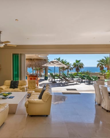 Open-plan living and dining room with ocean view, yellow leather seating, and direct access to beachfront terrace with lounge chairs and umbrellas