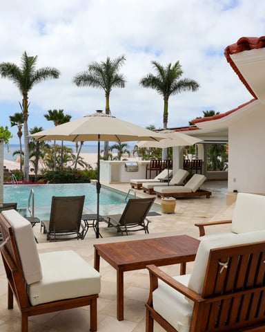 Beachfront villa patio with wooden furniture, pool, palm trees, and ocean view