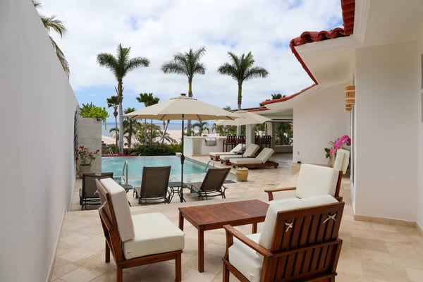 Beachfront villa patio with wooden lounge chairs, pool, palm trees, and ocean view