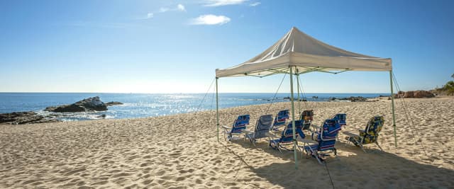 Beige canopy tent with blue beach chairs on sandy beach overlooking calm ocean and rocky coastline