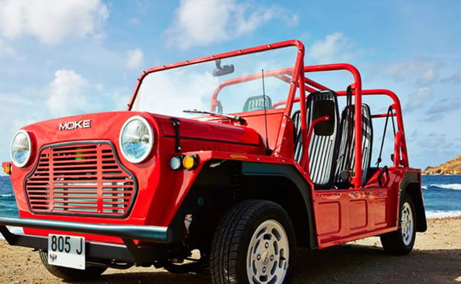 Red vintage Moke vehicle parked on beach with ocean and blue sky in background