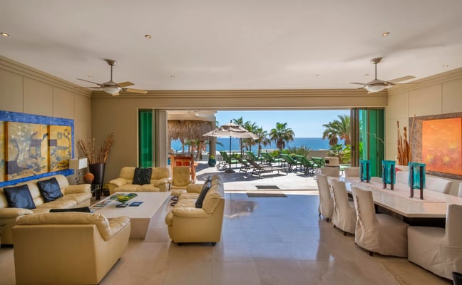 Open-plan living and dining room with ocean view, yellow leather seating, and direct access to beachfront terrace with lounge chairs and umbrellas