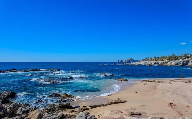 Sandy beach with rocky outcrops, turquoise water, and coastal cliffs under clear blue sky