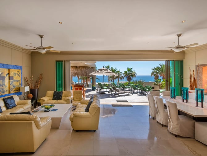 Open-plan living and dining room with ocean view, yellow leather seating, and direct access to beachfront terrace with loungers and umbrellas