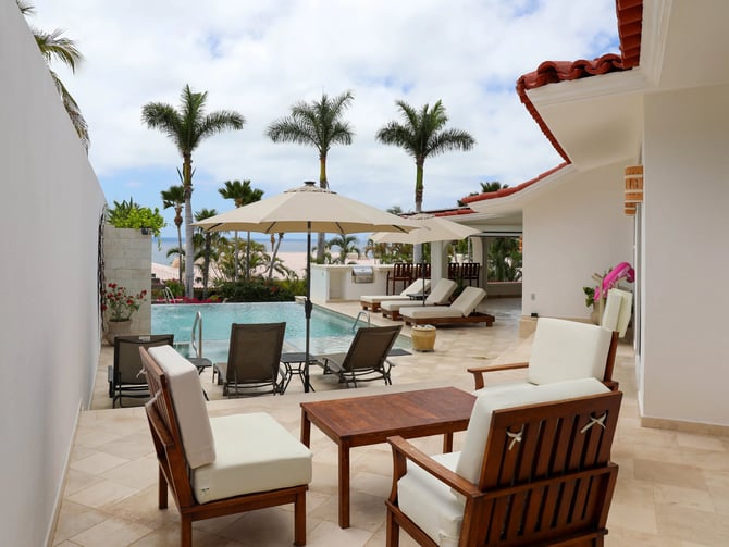 Beachfront villa patio with wooden lounge chairs, pool, palm trees, and ocean view